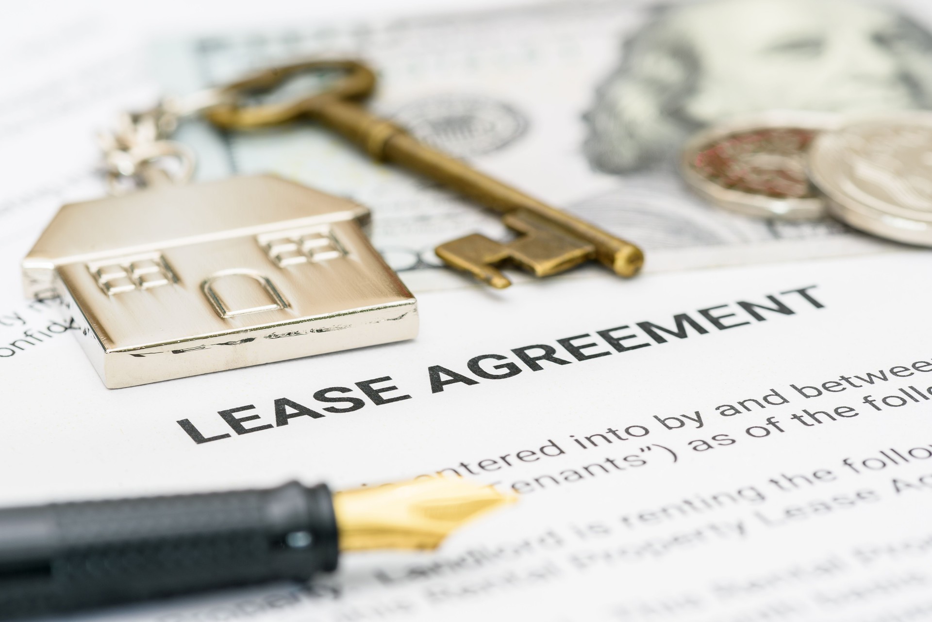Property rental, leasing contracts, real estate, housing agreements, and property management. A close-up view of a lease agreement document with a house key, coins, US dollar, and a pen placed on top.
